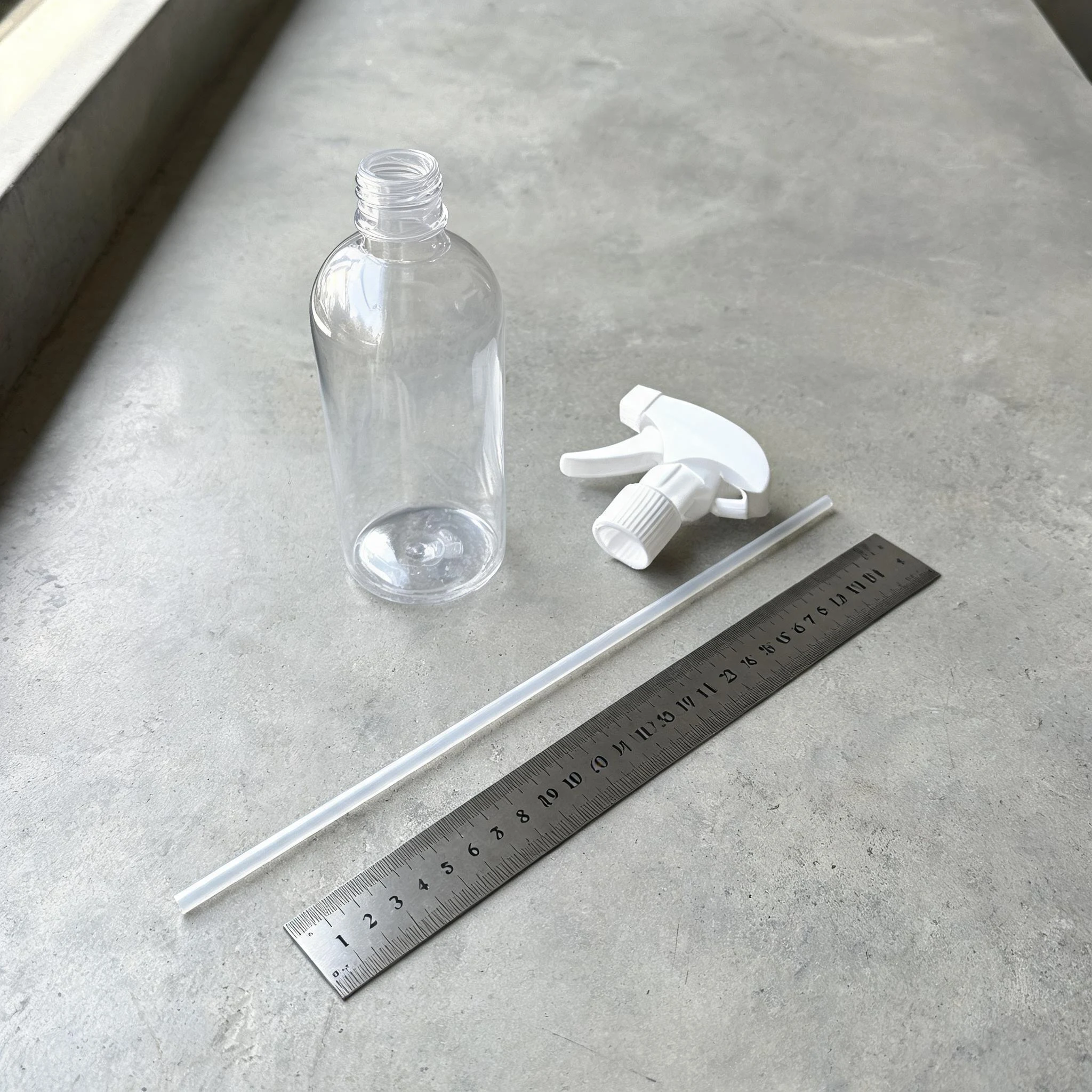 Tube plongeur posé le long d'une règle en acier près d'un flacon spray transparent